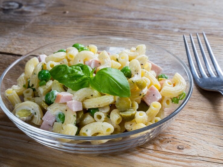 Durchsichtige Schale gefüllt mit Nudelsalat mit Fleischwurst und Erbsen. 