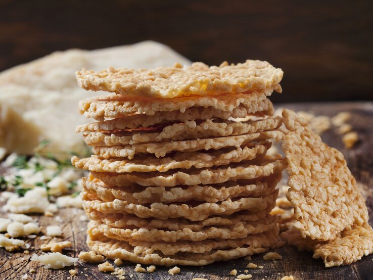 Stapel gebackene Käse-Cracker auf Holzbrett vor dunklem Hintergrund. 