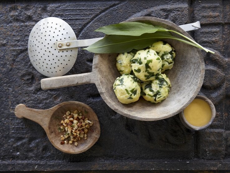 Die Bärlauch-Kartoffelknödel in einer weißen Marmorschale mit der Sauce Bernaise auf einem dunkelgrauem Untergrund.