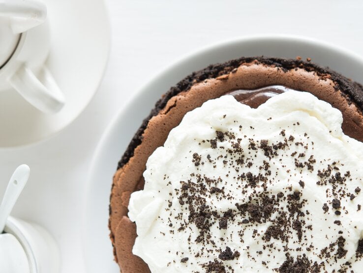 Schokoladenkuchen mit Sahne-Topping auf weißem Untergrund. 