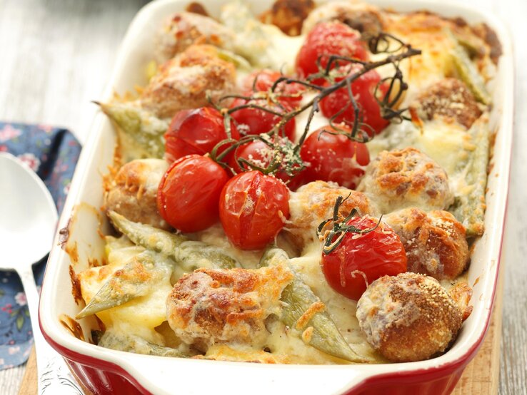 Kartoffelauflauf mit Hackbällchen und Tomaten in weißer Auflaufform. 