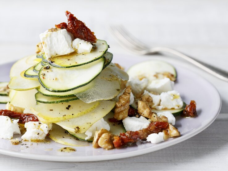 Ein  Teller belegt mit Birnen-Salat mit Zucchini, Ziegenfrischkäse und Walnüssen.