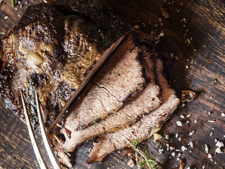 Der angeschnittene Rinderbraten auf einem Holzbrett direkt von oben fotografiert.