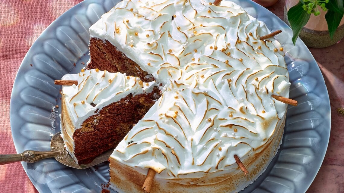 Zimtstern-Marmorkuchen mit Baiserhaube auf einem blauen Teller auf rosa Hintergrund. 