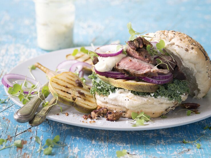 Der Burger auf einem weißen Teller mit hellblauem Tisch von der Seite fotografiert.