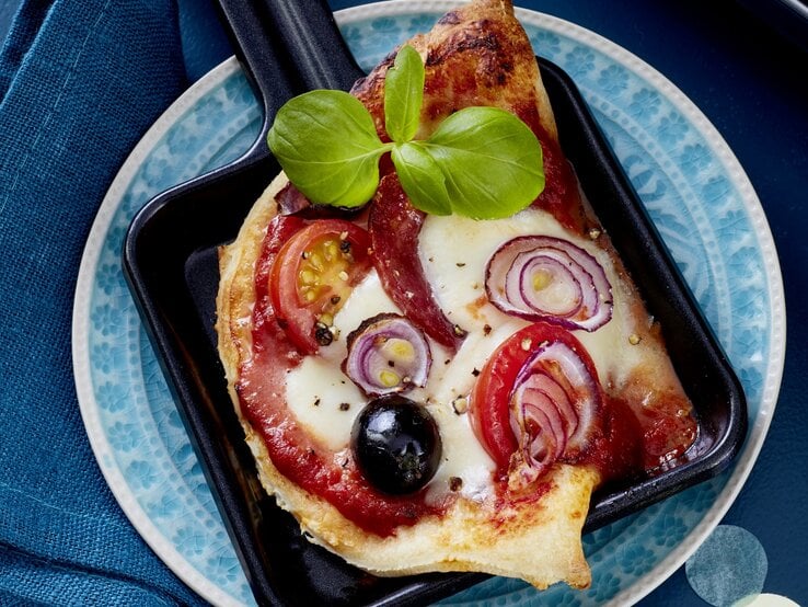 Salami-Pizza-Pfännchen auf einem blauen Teller auf blauem Hintergrund. 