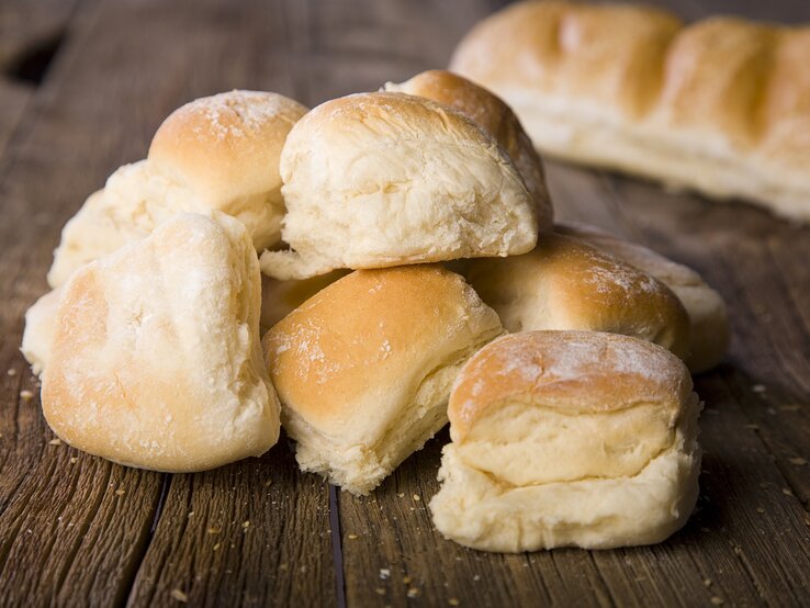 Mehrere goldbraune Quarkbrötchen sind auf einem Holztisch gestapelt, mit einem weiteren Brotlaib im Hintergrund.