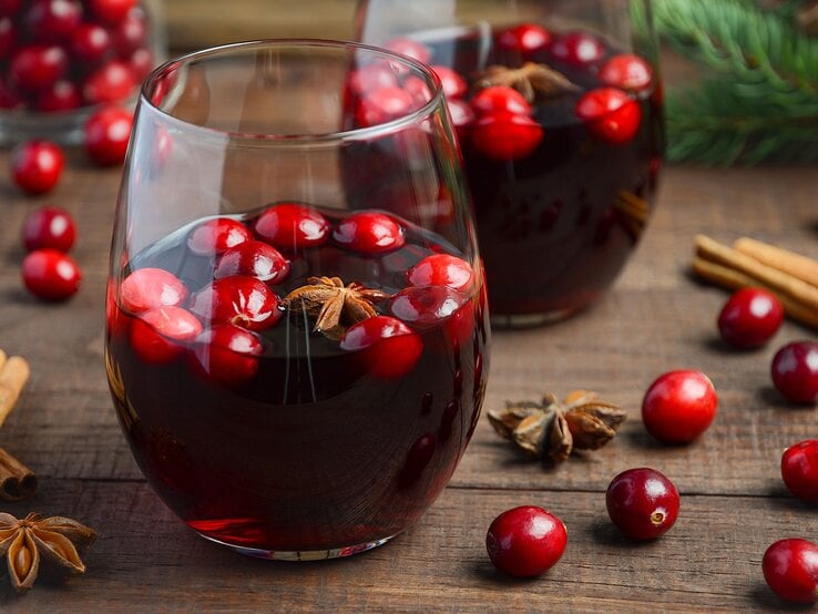 Ein Holztisch mit zwei Gläsern und Glühwein nah fotografiert. im Hintergrund Tannenzweige und Weihnachtsdeko.