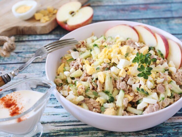Thunfischsalat mit Ei. Cremiger Salat aus Ei, Thunfisch und Gurken, mit Apfelscheiben und Kräutern garniert, serviert auf einem Holztisch.