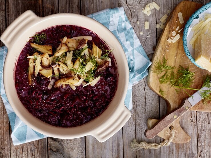 Rote Bete Risotto auf hölzernem Hintergrund. Rechts davon Parmesan.