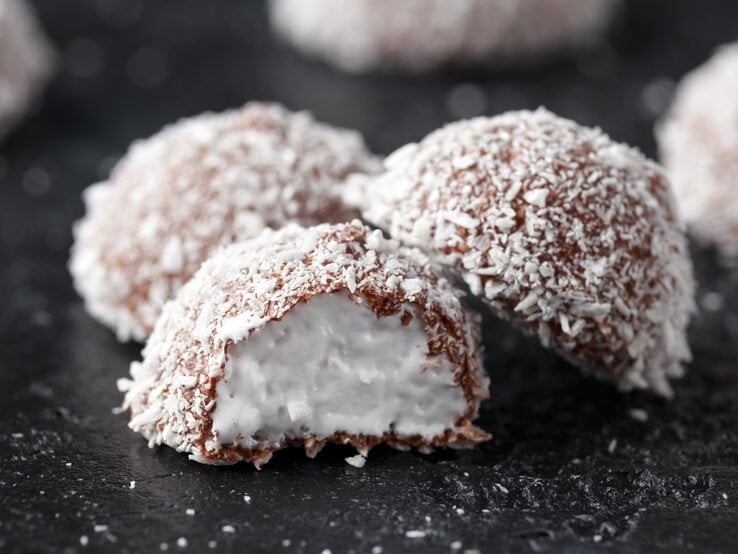 Schokoladenpralinen mit Kokosraspel bedeckt auf dunklem Untergrund.