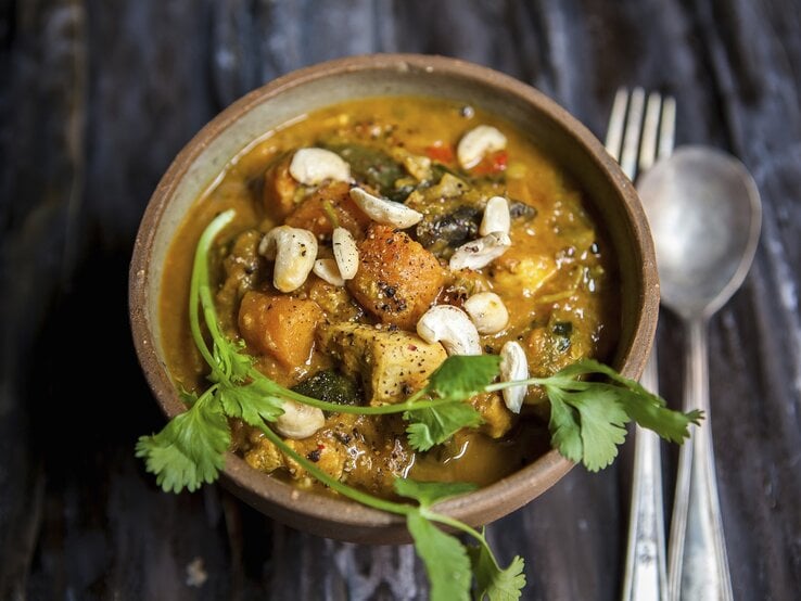 Süßkartoffel-Curry mit Hähnchen Cremiges Süßkartoffel-Curry mit Hähnchen und Cashews, garniert mit frischem Koriander in einer Schale auf dunklem Holztisch.