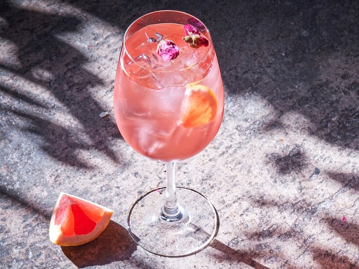 Ein Glas Pink Spritz auf ein er Betonfläche von schräg oben fotografiert.