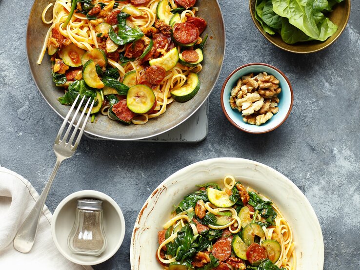 Linguine mit Chorizo und Zucchini auf eine grauen Telle ru ddunklem Tisch direkt von oben fotografiert.