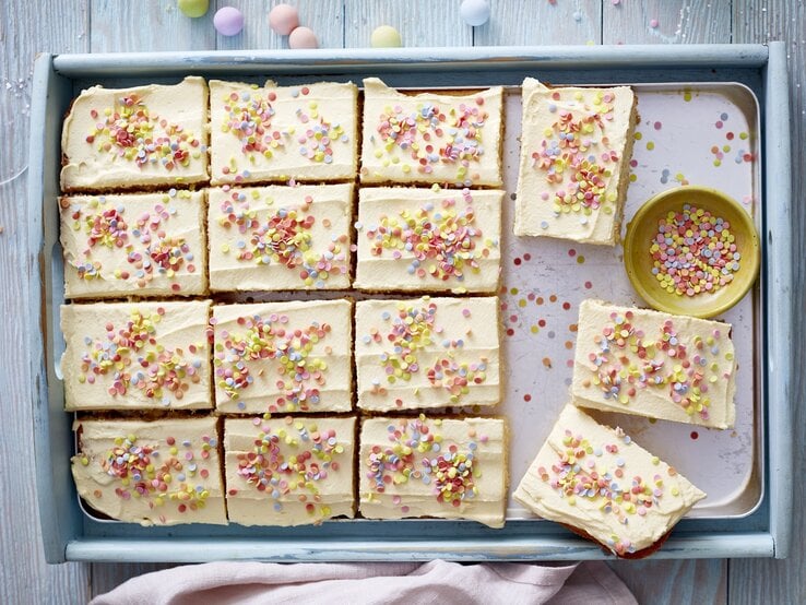 Konfetti-Kuchen auf einem Backblech auf einem hellblauen Hintergrund. Auf dem Hintergrund Konfetti verteilt. 