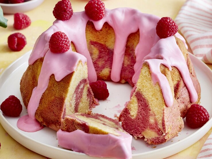 Rosa Marmor-Gugelhupf mit Himbeeren auf weißem Teller auf gelben Untergrund, Frontalaufnahme