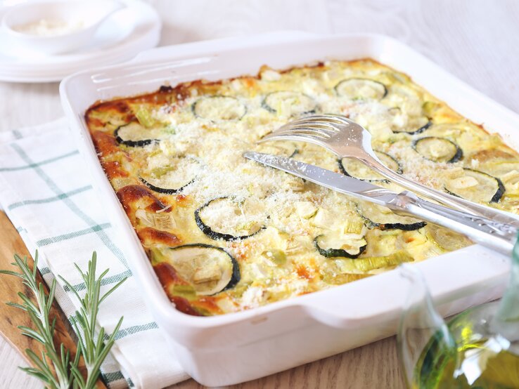 Auflaufform gefüllt mit Zucchini-Auflauf angerichtet auf mediterranem Geschirrtuch. 