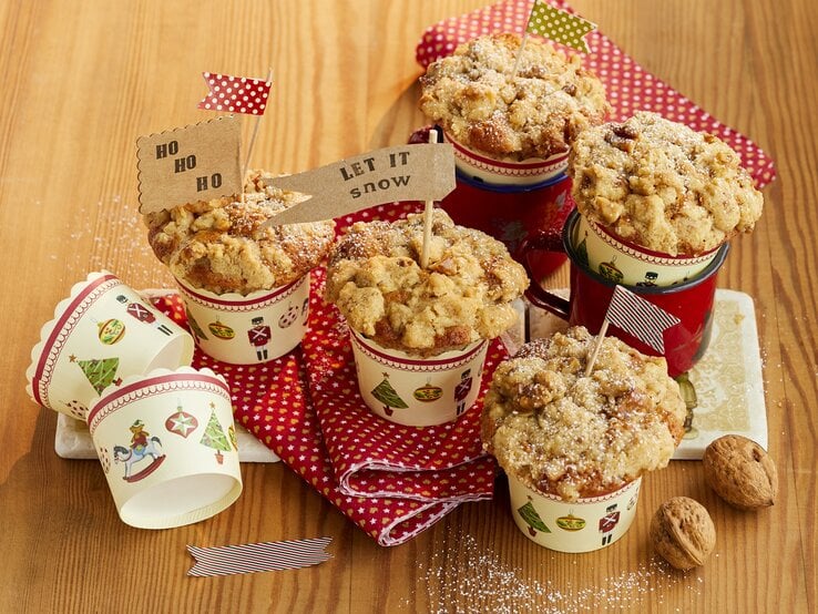 Bratapfel-Walnuss-Muffins auf einem hellen Holztisch mit roter Tischdecke. Alles von schräg oben fotografiert.