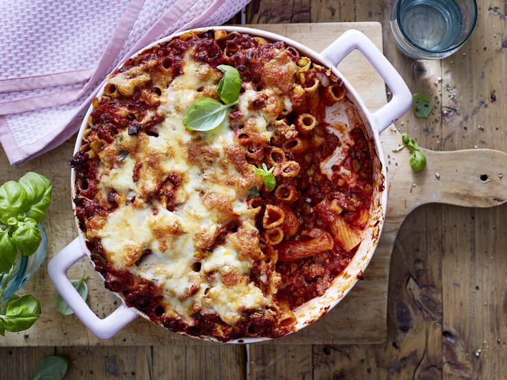 Rigatoni-Auflauf mit Hacksoße in einer weißen Auflaufform auf einem Holzbrett.