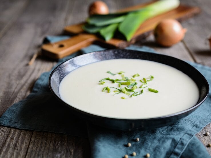 Ein schwarzer Suppenteller gefüllt mit einer cremigen, pürierten Lauchsuppe. 