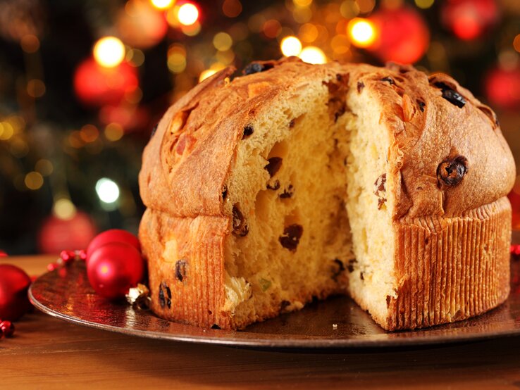 Angeschnittener Panettone vor weihnachtlichem Ambiente. 