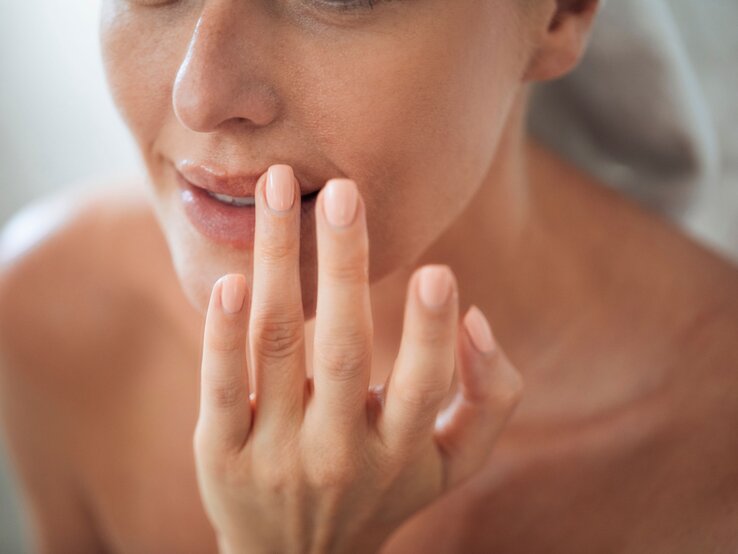 Nahaufnahme des unteren Teils des Gesichts einer Frau, die sanft ihre Wange mit der Fingerspitze berührt. | © Shutterstock/LStockStudio