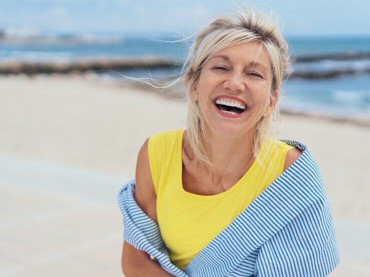 Dame mittleren Alters steht lachend am Strand