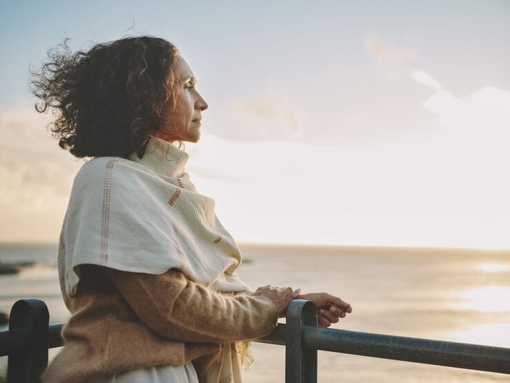 Eine Frau steht am Strand und guckt in den Sonnenaufgang über dem Meer.