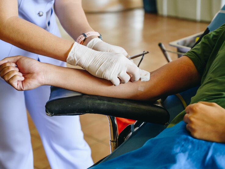 Es sind zwei Personen zu sehen. Eine Person liegt und spendet Blut, die andere setzt den Zugang.