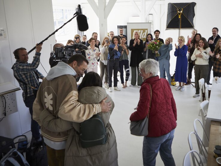 Eine Gruppe applaudierender Menschen umringt ein Paar, das sich umarmt, während ein Kamerateam die Szene filmt. | © dsphotos.de