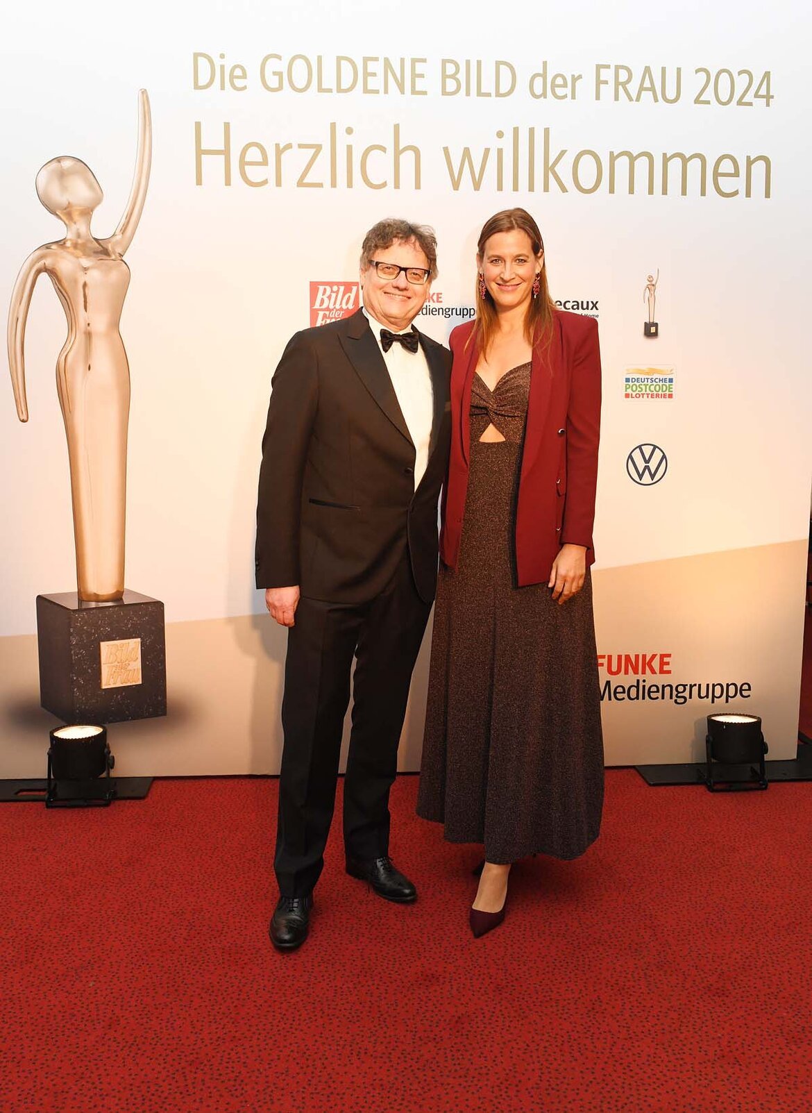 Elegant gekleidetes Duo posiert auf einem Gala-Event vor einer goldenen Trophäe und einer Wand mit dem Schriftzug "Goldene Bild der Frau 2024" | © BILD der FRAU 