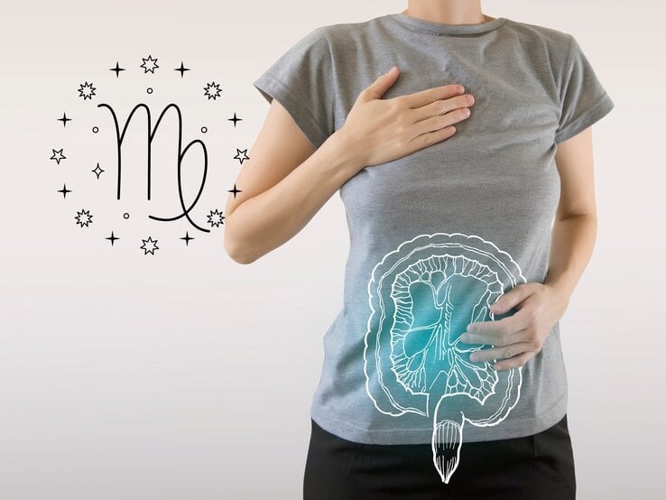 Das Bild zeigt eine Frau in einem grauen T-Shirt, die eine Hand auf ihre Brust und die andere auf ihren Bauch legt. Auf ihrem Bauch ist eine schematische Zeichnung des Verdauungssystems zu sehen, die auf das T-Shirt projiziert ist. Links neben ihr ist das astrologische Symbol für Jungfrau (Virgo) umgeben von kleinen Sternen abgebildet.