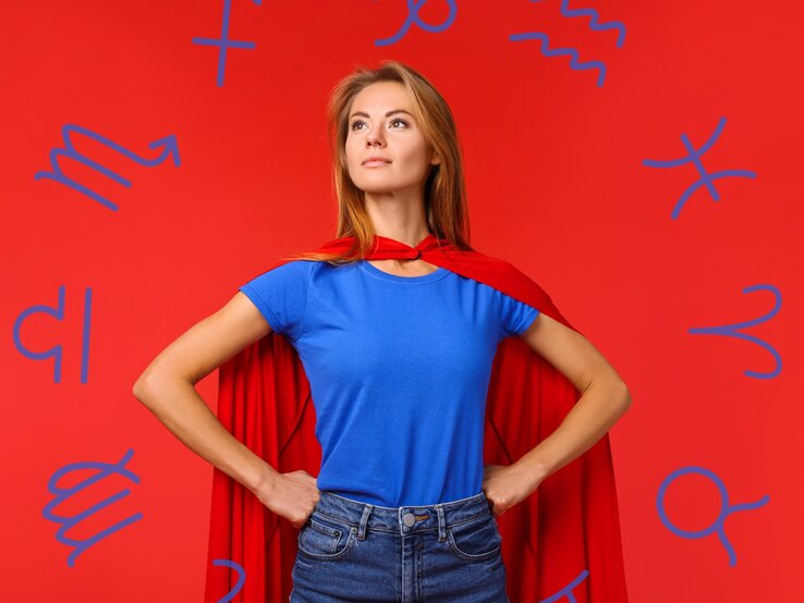 Eine Frau in einem blauen T-Shirt und rotem Umhang steht in einer kraftvollen Superhelden-Pose vor einem roten Hintergrund. Sie schaut entschlossen in die Ferne. Um sie herum schweben Symbole der Tierkreiszeichen, was eine Verbindung zwischen Stärke, Selbstbewusstsein und astrologischen Eigenschaften andeutet. Die Szene vermittelt ein Gefühl von Macht, Unabhängigkeit und Selbstvertrauen.