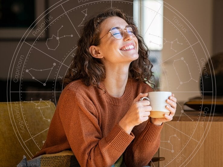 Eine lächelnde Frau mit lockigem Haar und Brille sitzt entspannt auf einem Sofa, hält eine Tasse in den Händen und genießt den Moment. Im Hintergrund ist ein astrologisches Rad mit den Sternzeichen zu sehen, was auf eine positive Verbindung zwischen ihrem Glück und astrologischen Einflüssen hinweist.