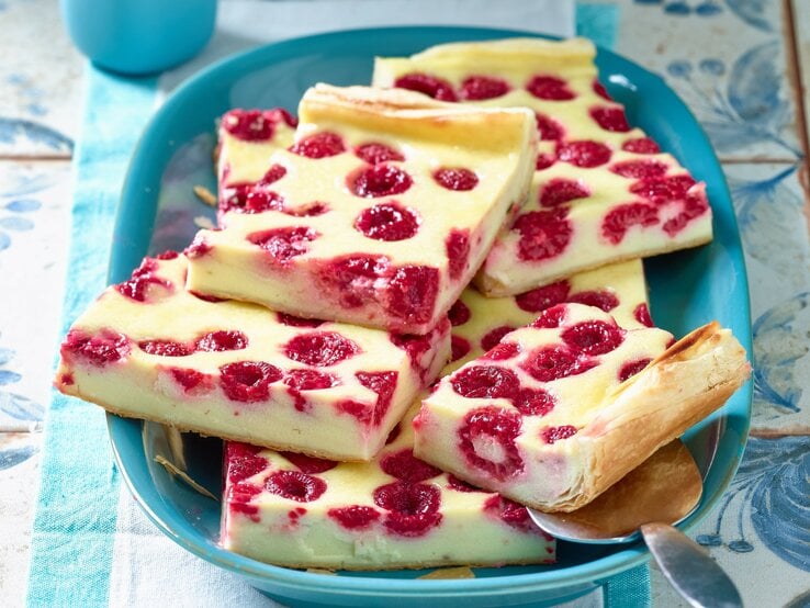 Türkisfarbener Teller mit Stücken von Himbeer-Käsekuchen, appetitlich angerichtet auf rustikalem Untergrund.