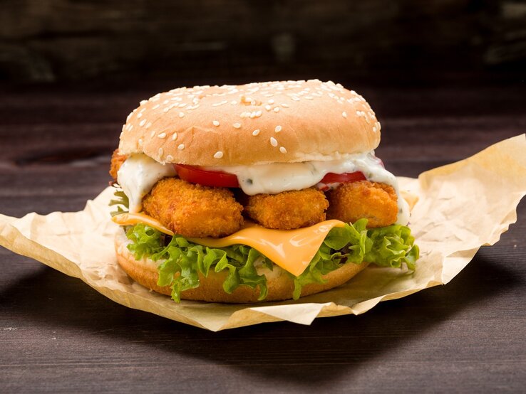 Der Fischstäbchen-Burger auf einem dunklen Tisch und schwarzem Hintergrund. Alles nah und von der Seite fotografiert