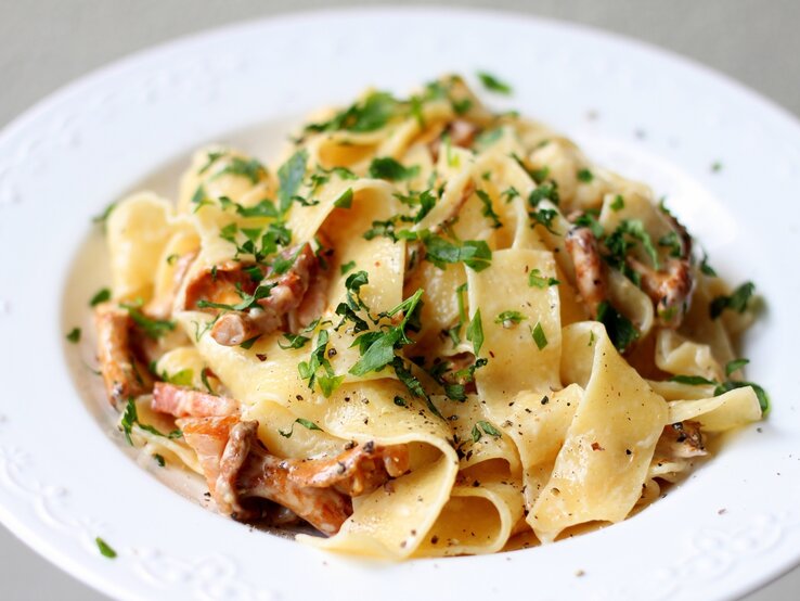 Ein weißer Teller auf weißem Untergrund mit der Pasta. Alles sehr nah und detailliert fotografiert.