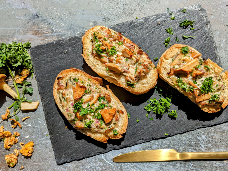 Drei Brötchenhälften mit der Flammkuchenfüllung und Pfifferlingen. Alles auf einer Schiefertafel und grauem Tisch direkt von oben fotografiert.