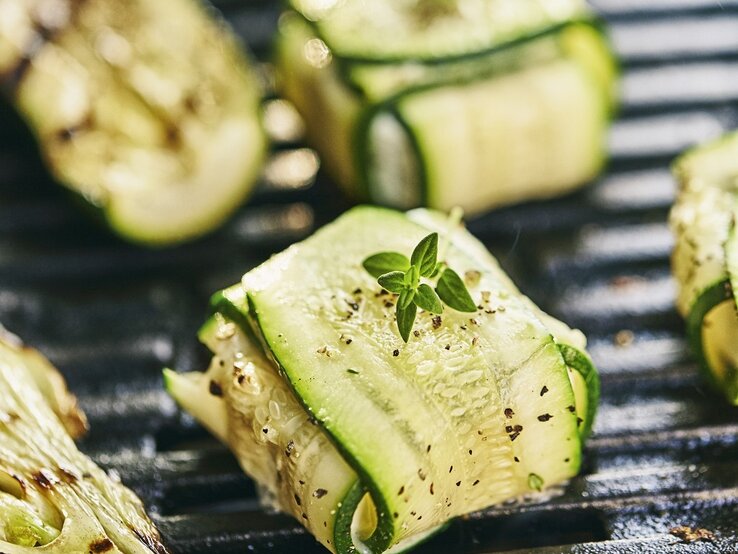 Gegrillte Zucchiniröllchen mit frischen Kräutern auf einem heißen Grill, leicht gewürzt und dampfend.