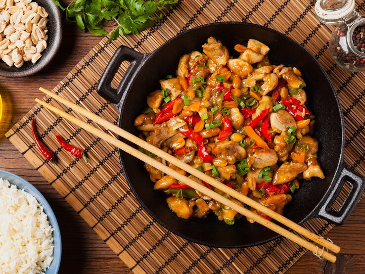 Ein Teller mit dem Wok-Gericht auf einem dunklen Tisch mit asiatischen Deko-Elementen direkt von oben fotografiert.