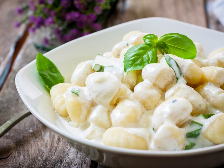 Ein weißer Teller befüllt mit Low-Carb-Gnocchi in cremiger Soße auf Holztisch.