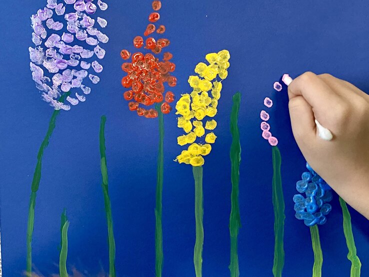 Kinderhand malt bunte Blumen mit Wattestäbchen auf dunkelblauem Hintergrund