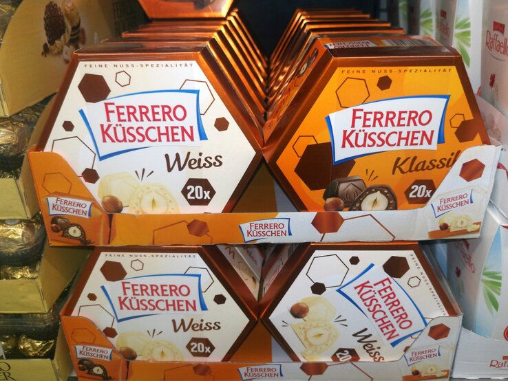 Verschiedene Sorten Ferrero Küsschen in orange-braunen Verpackungen auf einem Verkaufsdisplay im Supermarkt.
