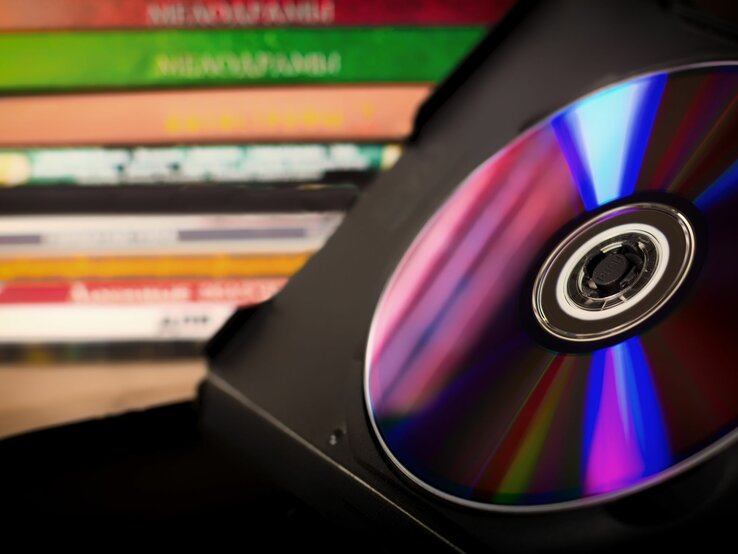 Eine glänzende CD in einer schwarzen Hülle, im Hintergrund befinden sich weitere DVDs gestapelt.