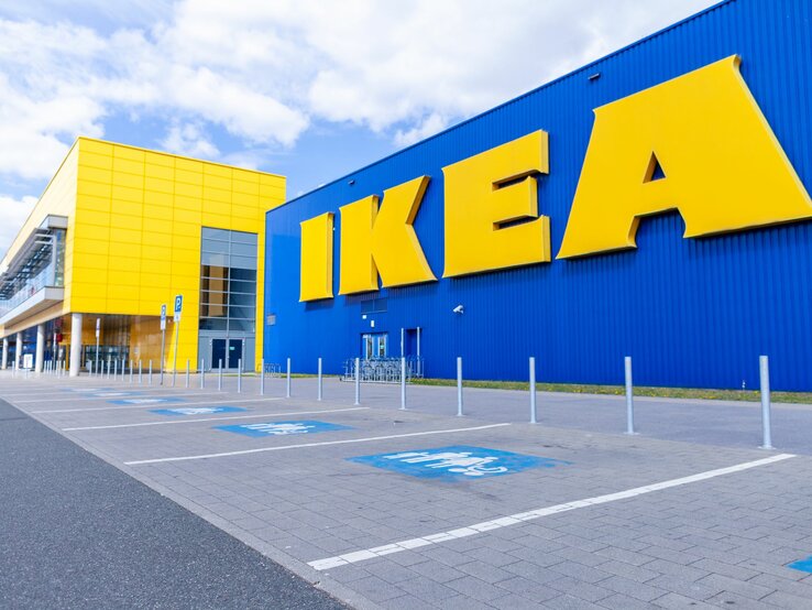 Blick auf ein modernes IKEA-Gebäude mit großer blauer Fassade und gelben Buchstaben an einem sonnigen Tag.