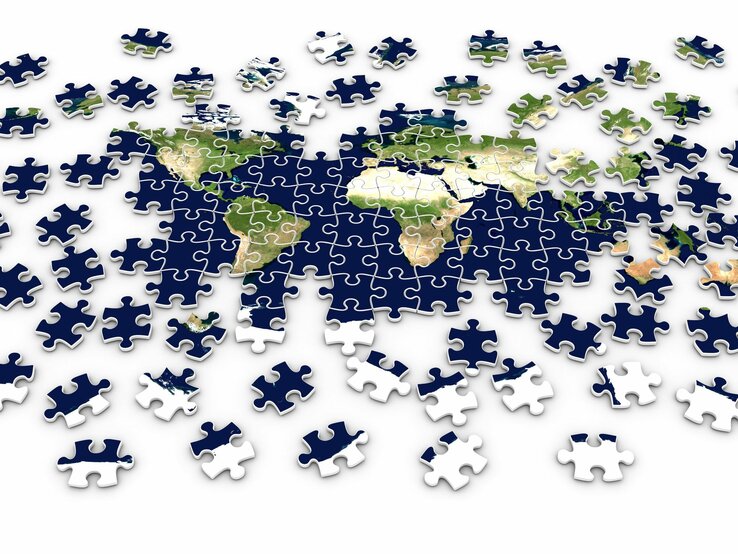 Ein teilweise fertiggestelltes Puzzle zeigt die Weltkarte mit verstreuten, noch nicht platzierten Puzzleteilen.