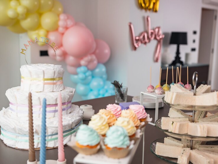 Ein Tisch mit einer Windeltorte, bunten Cupcakes, Sandwiches und Cake-Pops bei einer Babyparty mit Luftballon-Dekoration.