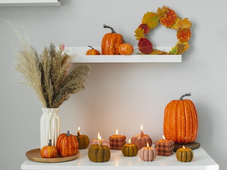 Herbstliche Dekoration mit Kürbissen, brennenden Kerzen in Kürbisform, einem Trockenblumenstrauß und einem Blattkranz.