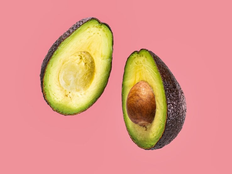 Zwei Hälften einer reifen Avocado, eine mit Kern, liegen vor rosa Hintergrund nebeneinander. Mit Kern und Schale kann man basteln.