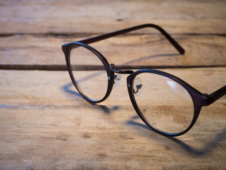 Schwarze Brille mit runden Gläsern liegt auf einem rustikalen Holztisch in weichem, natürlichem Licht.